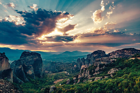 View of towering rock formations amidst the verdant landscape, kissed by golden sunlight piercing through the dramatic clouds in the sky, Kalabaka, Trikala, Greece.