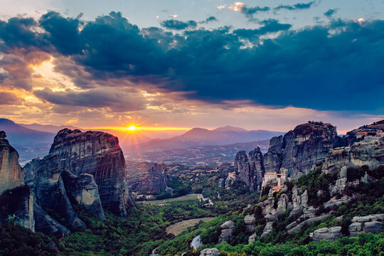 View of towering rock formations amidst lush greenery bathed in the warm glow of the setting sun, a serene landscape painted with vibrant colors, Kalabaka, Trikala, Greece.