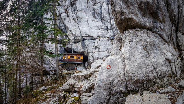 View of a cozy wooden cabin nestled within the rugged embrace of a rocky cave, a testament to human ingenuity against nature's grandeur, Jasenak, Karlovac County, Croatia.