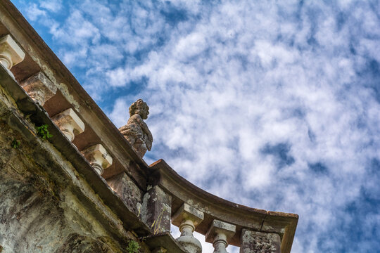 View of weathered stone balustrade with ornate carvings reaching towards a vibrant blue sky dotted with fluffy white clouds, Pontremoli, Tuscany, Italy.