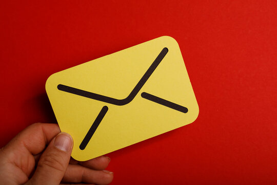 A hand holding a bright yellow email illustration against a red background, perfect for communication concepts.