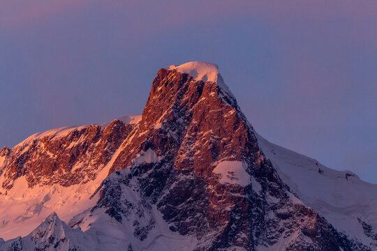View of jagged, snow-dusted peaks pierce the pastel sky, bathed in the warm, rosy glow of the setting sun, Hunza Nagar, Gilgit, Pakistan.