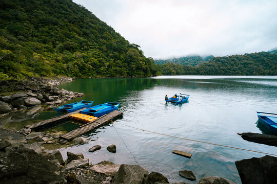 View of tranquil waters reflect the verdant hills as bright blue boats bob gently near a rocky shore, inviting exploration, Sibulan, Central Visayas, Philippines.