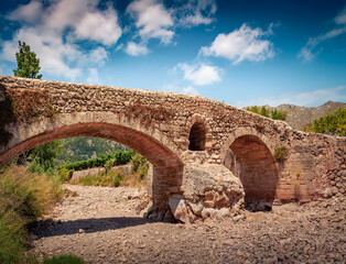 Bright summer view of Roman bridge across the Torrent de Sant Jordi river. Splendid morning scene of Pollenca cityscape, Majorca, Balearic islands, Spain, Europe. Traveling concept background.