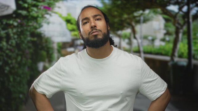 Man pointing finger on street with green foliage and trees, wearing white t shirt and beard visible, arm extended toward camera; anger.
