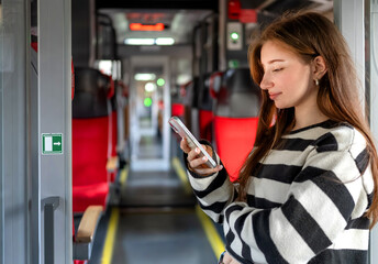 Fototapeta premium Young Woman Stands By The Train Exit Looking At Smartphone