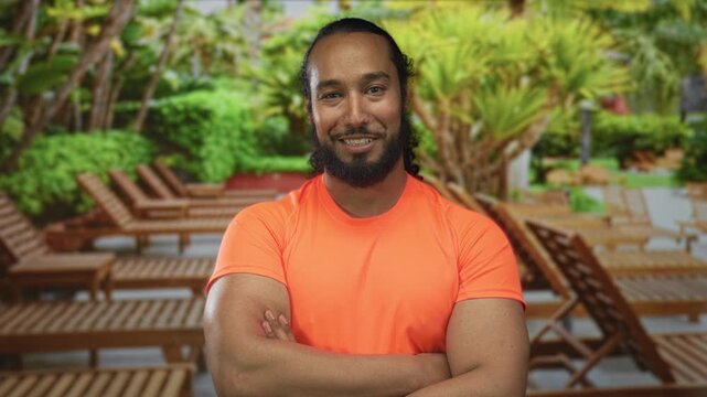 Man with arms crossed showing bare forearms and smiling in forest resort setting; confidence wellbeing.