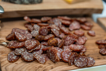 Fototapeta premium Thinly sliced salami with marbled fat rests on a rustic wooden board. Warm soft lighting and shallow depth of field suggest a luxury alpine hotel charcuterie station.