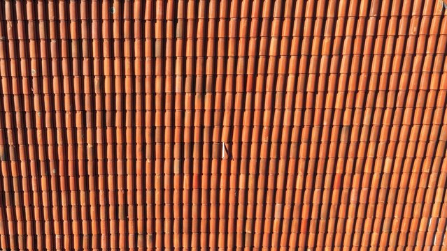 Drone aerial view of terracotta clay roof tiles forming a geometric pattern. Traditional ceramic roofing texture background on a residential building.