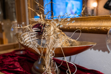 A gold centerpiece with metallic fern fronds, wire curls, and crystal droplets sits on a velvet console before a gilded mirror, warm ambient lighting suggests evening. © Aerial Film Studio