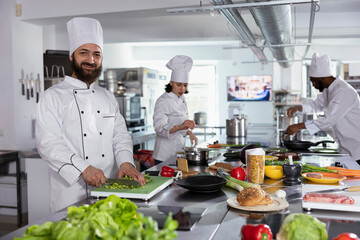 In a professional kitchen, male cook preparing gourmet meals by using cutting boards and chopping...