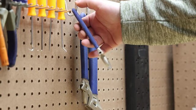 Hand reaching for adjustable wrench on pegboard tool organizer