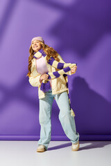 Obraz premium Young beautiful woman joyfully poses against a vibrant purple backdrop in stylish winter attire