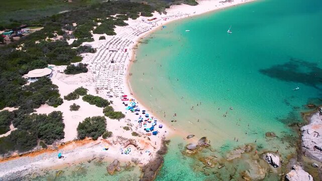 Sardinia Costa Rei Scoglio di Peppino aerial flight, large granite rock in turquoise sea, tropical white sand beach, cinematic drone reveal, Italy coastal scenery 4k