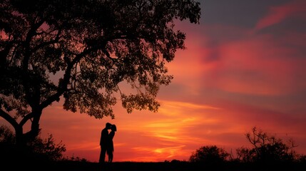 Fototapeta premium Couple embracing at fiery sunset beside large oak tree
