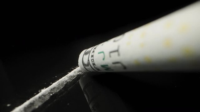 Imitation of cocaine use, close-up from a first-person view, white powder and one hundred dollar bill sucking up the powder on a black background.