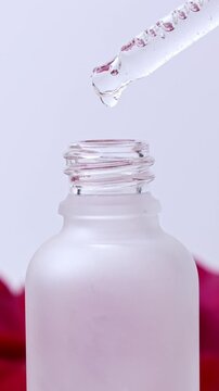 Cosmetics transparent liquid gel dripping from glass pipette into the bottle on white background, vertical video format