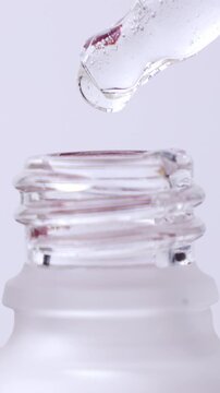 Cosmetics transparent liquid gel dripping from glass pipette into the bottle on white background, vertical video format
