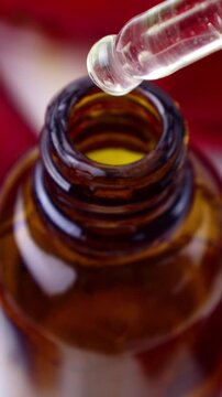 Cosmetic oil serum drops from the droplet with the bottle on red rose petals background, vertical video format