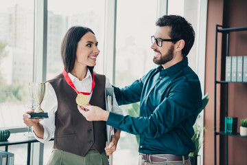 Business colleagues celebrate achievement as a woman receives a gold medal and trophy in a modern...