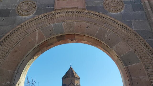 Saint Gayane Monastery․ A historic stone church with a distinctive conical roof, viewed through a stone archway, set against a clear blue sky