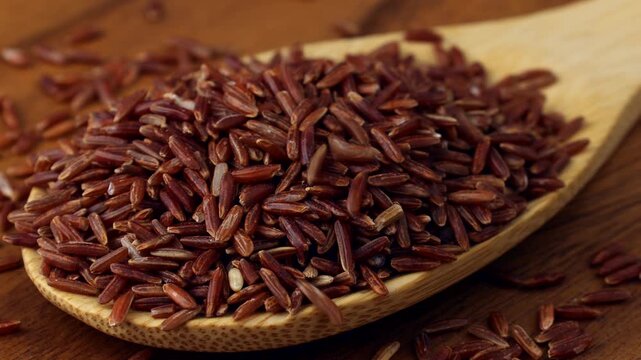 Thai Red Rice (Red Jasmine Rice) grains falling down into the wooden spoon close up