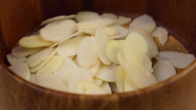 White almond petals falling down into the wooden bowl close up