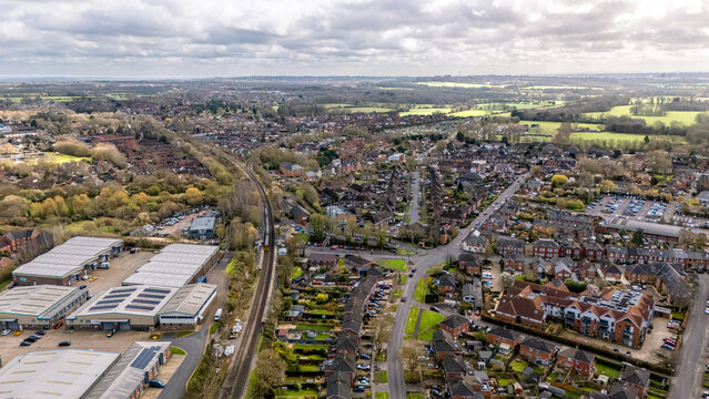 Landscape aerial drone shot overlooking Romsey, Hampshire with residential housing and railway track around quiet roads on overcast sunny spring day
