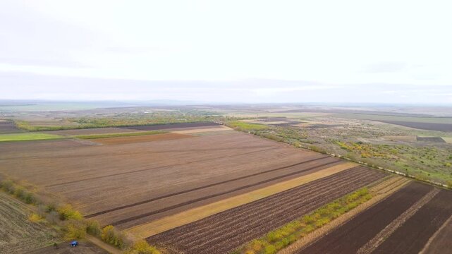 Rising aerial drone landscape of agricultural farmland and fields. High altitude drone view of large agricultural farmland fields stretching across rural countryside landscape.