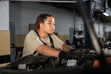 Fototapeta premium Dedicated female mechanic repairs a car in a bustling auto repair garage