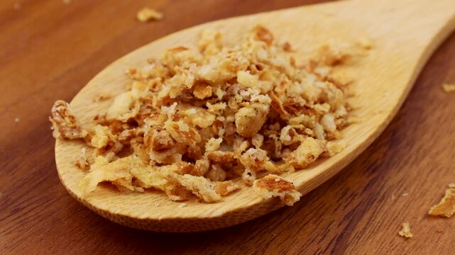 Organic crispy fried onions falling down into the wooden spoon close up