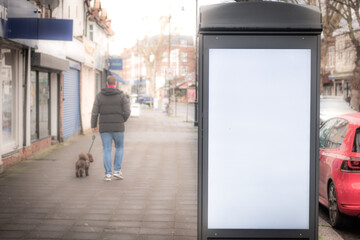 LONDON - Blank digital advertising kiosk on high street pavement with pedestrians