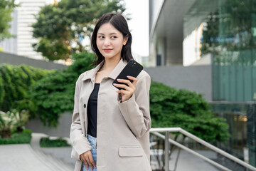 Fototapeta premium Beautiful business woman using mobile phone while walking business buildings. Smart female using cell phone chatting for business communication talking. Business lifestyle concept.