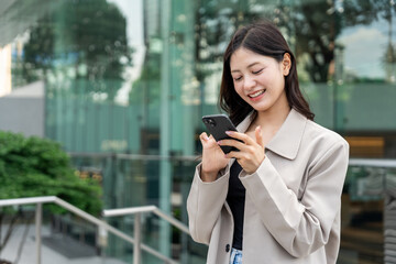 Fototapeta premium Beautiful business woman using mobile phone while walking business buildings. Smart female using cell phone chatting for business communication talking. Business lifestyle concept.