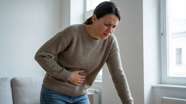 Adult woman suffering from stomach ache and digestive issues while standing at home