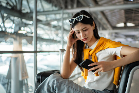 Unhappy young woman traveler disappointed with flight delay or cancelation while waiting at airport terminal, female tourist upset after receiving bad news when sitting at airline lounge.