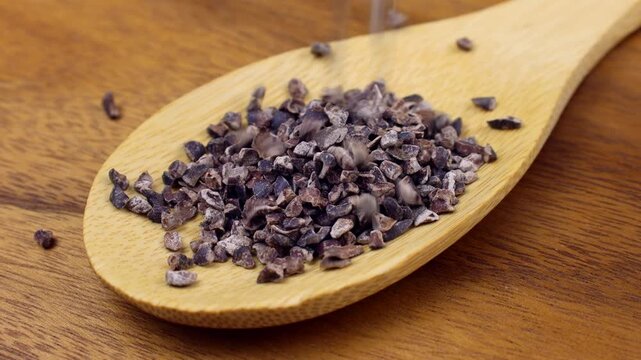 Roasted brown crushed cocoa nibs falling down into the wooden spoon close up