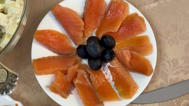Red trout slices with olives plated on white porcelain plate arranged in floral pattern with light salt sprinkle beside vintage.