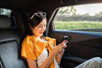 Naklejka premium Relaxing moment of beautiful woman sitting in car back seats with safety belt and look out in the window. Female happy in car while traveling on the road to your destination.