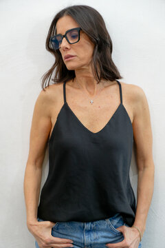 Woman in a black camisole and denim jeans looking down against a white wall. Milan, Italy