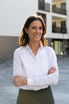 Woman smiling with arms crossed, standing outdoors in front of a modern building. Milan, Italy