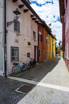 Charming colorful alley with bikes parked against the wall under a cloudy blue sky.  Caorle, Metropolitan City of Venice, Veneto, Italy