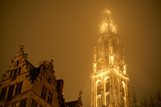 Illuminated Gothic cathedral tower against a misty night sky in Antwerp Zurich, Switzerland