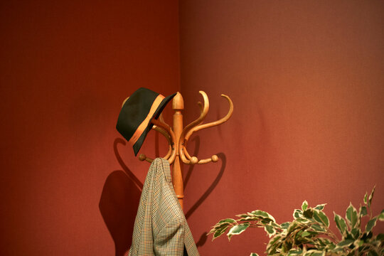 A fedora and checkered coat hang on a wooden coat rack against a red wall with a green plant. Brussels, Belgium