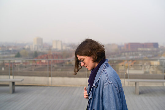 Young woman in a denim jacket on a rooftop with a cityscape in the background. Brussels, Belgium