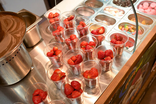 Counter with multiple cups filled with fresh strawberries alongside toppings and melted chocolate. Brussels, Belgium