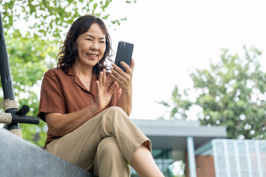 Happy senior woman using smartphone for video call in green garden with digital technology engagement lifestyle, smiling elderly female greeting online connection with family in wellbeing retirement