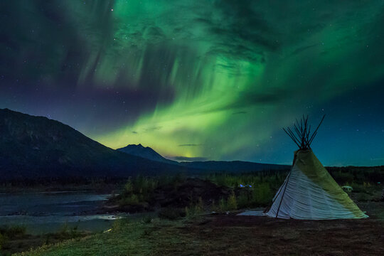 Northern lights illuminate a tent in a scenic wilderness under a starry sky. Wrangell St. Elias National Park, Alaska, USA