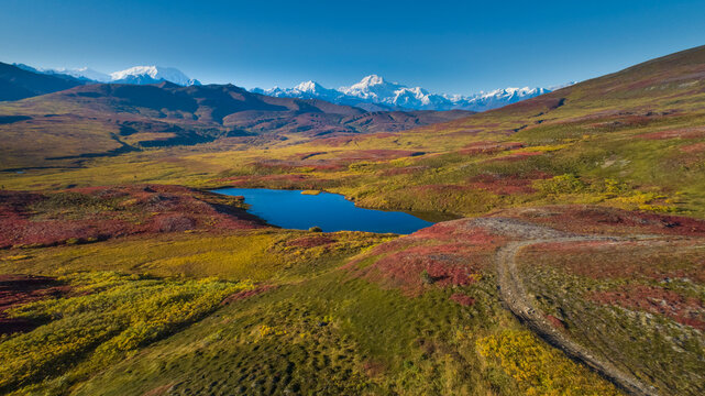 Aerial view of colorful autumn tundra landscape with a vibrant lake and distant snowy peaks. Wrangell St. Elias National Park, Alaska, USA