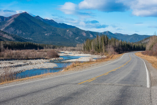 Winding road with mountain backdrop and scenic river under blue sky. Montana, USA
